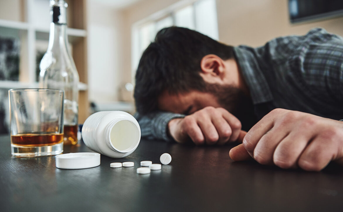 Alcoholism and drug addiction are killer of mental and physical health. Drunk man at table with alcohol and drugs. Alcoholism concept