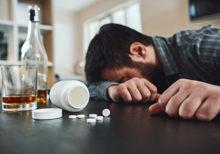 Alcoholism and drug addiction are killer of mental and physical health. Drunk man at table with alcohol and drugs. Alcoholism concept