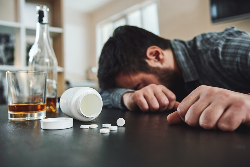 Alcoholism and drug addiction are killer of mental and physical health. Drunk man at table with alcohol and drugs. Alcoholism concept